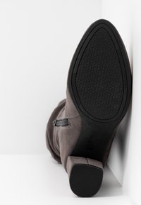 Bottine en daim gris avec un talon carré et une fermeture éclair latérale, dotée d'une semelle extérieure en caoutchouc noir texturée avec logo embossé.