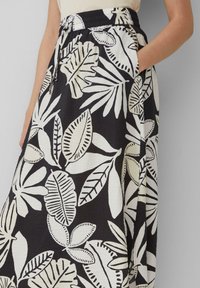 Jupe noire avec des motifs de feuilles blanches, taille élastique avec cordon de serrage et poches latérales. Le tissu a une finition texturée.