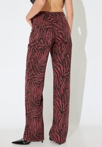 Pantalons ample en bordeaux avec un motif de rayures zèbres noires. Tissu en coton avec une texture lisse et deux poches arrière.