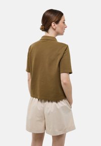 Polo shirt marron à manches courtes avec un col classique, associé à un short beige clair. La chemise a un design court et une texture lisse.