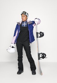 Skiklær bestående av en marineblå og rosa isolert jakke, svarte overaller og svarte støvler. Holder et snowboard med bindinger og en hjelm.