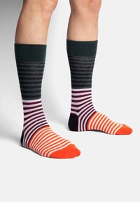 Calcetines coloridos con una parte superior acanalada de color verde oscuro, que presentan patrones horizontales y rayas contrastantes en púrpura, negro, naranja y blanco.