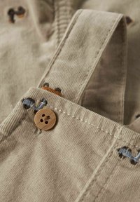 Beige corduroy tuinbroeken met geborduurde dierenmotieven, voorzien van een houten knoopsluiting en textuurdetails op de banden.