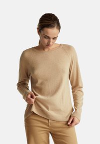 Beżowy sweter z długim rękawem o okrągłym dekolcie i prążkowanym wykończeniu. Wykonany z miękkiego materiału o gładkiej teksturze i rękawach raglanowych.