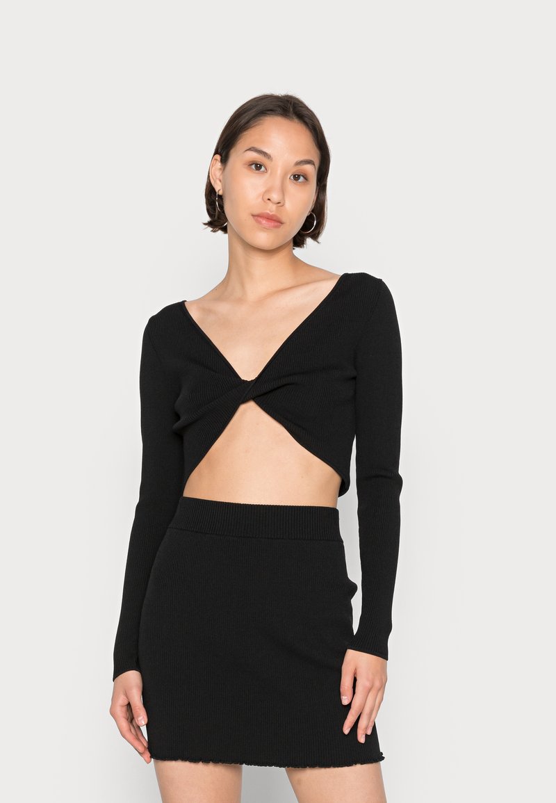 Conjunto preto de duas peças com uma blusa ajustada de mangas longas, decote em V profundo e frente torcida, combinada com uma saia mini correspondente.
