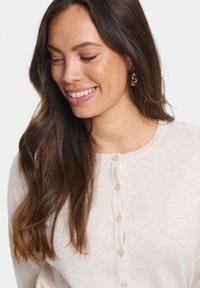 Svetlo bež zimska jopica s kroženjem, diskretno rebrasto teksturo in šestim malim gumbi spredaj.