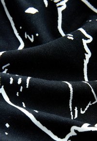 Crni materijal s bijelim apstraktnim linijama, prikazuje glatku teksturu i meki pad, naglašavajući kontrastne boje i uzorke.