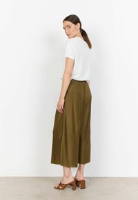 T-shirt bianco a maniche corte abbinato a culotte plissettate verde oliva, con cintura elastica e sandali con tacco marroni.