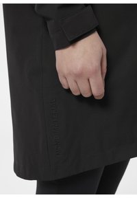 Czarny płaszcz wykonany z teksturowanej tkaniny, z mankietami i wyszywaną detalem "MONO MATERIAL" wzdłuż boku.