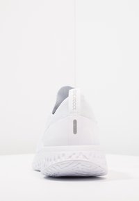 Baskets blanches de sport avec une tige texturée, col intégré semblable à une chaussette et semelle rembourrée. Présente un accent réfléchissant près du talon.