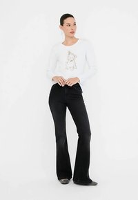 Balta garām piedurknēm krekls ar zirga grafiku un ziedu detaļām, kopā ar melnām zvana piegriezuma džinsu biksēm. Tumši apavi noslēdz apģērbu.