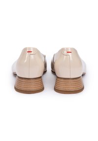 Beige patent leather shoes with a low stacked heel, featuring a red accent at the back and a smooth, shiny texture.