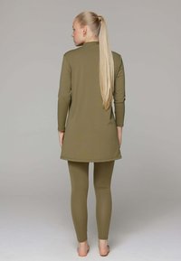 Olijfgroene tuniek met lange mouwen, reikt tot halverwege de dijen, gecombineerd met bijpassende legging. Gladde, rekbare stof met een eenvoudig ontwerp.