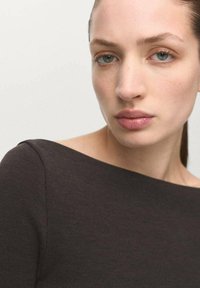 Bruin geribd topje met een brede halslijn en een aansluitend ontwerp, dat een gladde textuur en subtiele naden benadrukt, gedragen door een persoon tegen een neutrale achtergrond.