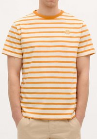 Camiseta a rayas con franjas horizontales naranjas y blancas. Cuello redondo, material de algodón suave, parche de logo en el pecho, corte relajado.
