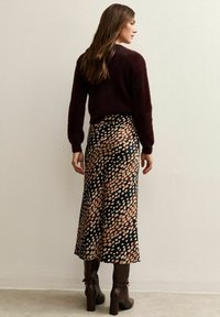 Bordeaux fuzzy sweater gecombineerd met een zwarte rok met een kleurrijk gemêleerd patroon en bruine haklaarzen. Het achteraanzicht legt de nadruk op het ontwerp.