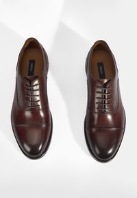 Chaussures habillées en cuir marron avec une finition lisse, un bout rond et un design à lacets. Présentent des coutures décoratives et une légère brillance.