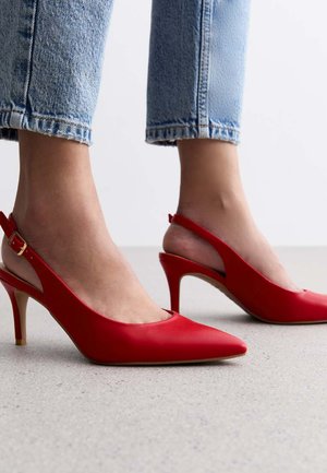 Red slingback high heels with a pointed toe, made of smooth leather, featuring a slim heel and gold buckle accents. Worn with light blue denim.