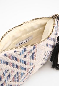 Pochette texturée en crème, avec des motifs triangulaires en bleu et rouge. Fermeture éclair dorée et accent de pompon noir à l'intérieur. Intérieur doublé.