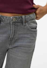 Jean en denim gris avec une taille mi-haute, doté d'une fermeture à bouton en métal, de poches avant et d'une texture légèrement délavée.