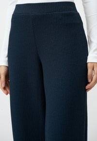 Navy geribde wijde broek met een textuurstof en een elastische tailleband, weergegeven naast een nauwsluitend wit langemouwen T-shirt.