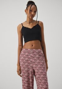 Top corto nero con bordi smerlati realizzato in tessuto morbido, abbinato a pantaloni larghi con motivo floreale nelle tonalità di rosa e bordeaux.