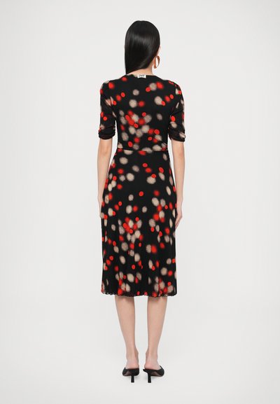 Musta mekko, jossa on keskipituinen leikkaus, punaisen ja beigen pistekuvio, lyhyet hihat ja yksinkertainen helma. Suunniteltu pehmeästä kankaasta.
