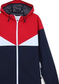 Giubbino rosso, bianco e navy con chiusura a zip, cappuccio regolabile e tasche laterali. Presenta un design a blocchi di colore e una texture liscia.