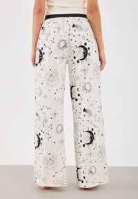 Leveälahkeiset housut kevyestä kankaasta, väriltään kerma, joissa musta taivaallinen kuvio auringosta, kuista ja tähdistä. Kuminauhavyötärö.