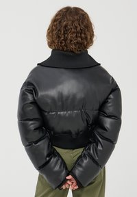 Giacca a vento nera in pelle lucida, vestibilità over size con colletto e polsini a coste neri. Caratterizzata da sezioni trapuntate e imbottite e orlo elastico.