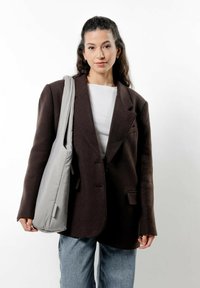 Przesadnie duża ciemnobrązowa marynarka z wyłogami, noszona na białej bluzce, w zestawieniu z jasnoniebieskimi dżinsami i jasnoszarym torbou na ramię.