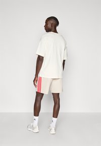 Μπλούζα κρεμ με κοντά μανίκια και μπεζ σορτς με κόκκινες ρίγες στο πλάι. Το μοντέλο φορά λευκά αθλητικά παπούτσια και κάλτσες μέχρι τον αστράγαλο. Νεανικό ύφασμα, άνετη εφαρμογή.