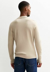 Beige Langarmpullover mit weicher Textur, gerippten Akzenten an den Bündchen und dem Saum, kombiniert mit dunkelblauen Denim-Jeans.