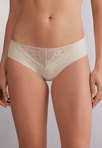 Béžové kalhotky s krajkovým lemem na horním předním okraji, hladká tkanina, střední výška pasu, s jemným květinovým vzorem na krajce.