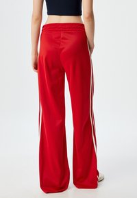 Rote Sporthose aus glattem Material, mit weißen Seitenstreifen, dehnbarem Bund und lockerer Passform.