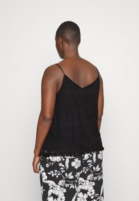 Black sleeveless top with thin straps, featuring a textured pattern and lace trim along the hem, paired with floral-patterned black and white pants.