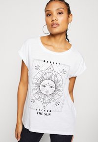 Hvit bomulls t-skjorte med svart grafisk design av solen og geometriske mønstre, med teksten "THE SUN" nederst.