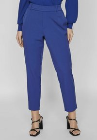 Pantalons taillés bleu avec une coupe ajustée, présentant une texture lisse et une taille mi-haute. L'ourlet est coupé juste au-dessus de la cheville.
