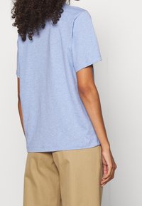 Camiseta de manga corta azul claro con una textura suave y un corte ligeramente holgado, combinada con pantalones beige. Presenta un escote redondeado y sencillo.