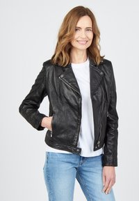 Svart lädermotorcykeljacka med asymmetrisk dragkedja, diagonala sömmar och sidofickor, tillsammans med en vit t-shirt och blå jeans.