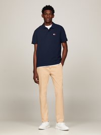 Polo de color marino con mangas cortas, ajuste slim. Combinado con pantalones beiges y zapatillas blancas. Detalle del logo en el lado izquierdo del pecho de la camiseta.