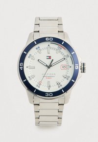 Silver Tommy Hilfiger wristwatch with white dial, blue bezel, date window at 3 o'clock, and metal link bracelet, showing time 11:10:35.