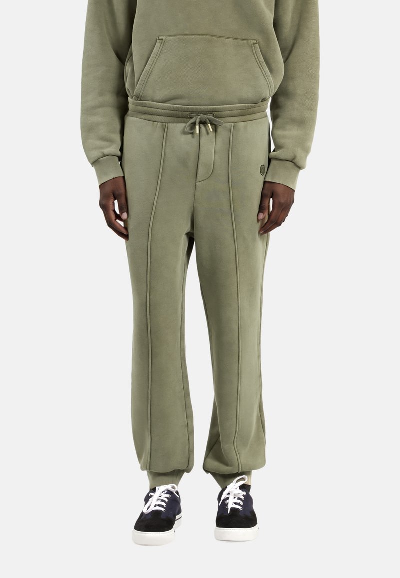 Groene fleecesweatpants met een trekkoord in de taille, zijnaden en afgewerkte enkels, gecombineerd met zwarte sneakers en witte veters.