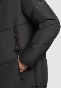 Schwarze gepolsterte Jacke mit glatter Textur, ausgestattet mit einem Frontreißverschluss, Seitentaschen und einer schrägen Reißverschlusstasche am Ärmel.
