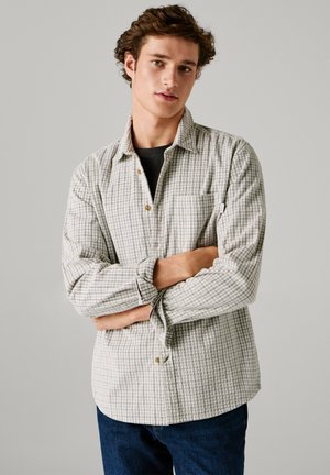 Heled halli ja valge ruuduline särk, millel on nööbid alla, rinna tasku ja pikad varrukad. Lahtine lõige ja puidust nööbid detaljina.