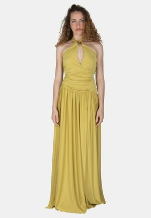 Donna con capelli ricci che indossa un abito lungo giallo con scollo a girocollo con apertura a goccia e vita arricciata, in piedi di fronte a uno sfondo semplice.