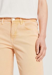 Jeans de mezclilla color melocotón con una textura suave, diseño de cinco bolsillos, costuras en contraste y cierre de botón en la cintura.