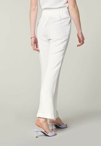 Bílé lněné kalhoty s volným střihem, s elastickým pasem a rovnými nohavicemi. V kombinaci se světle fialovými otevřenými podpatky.