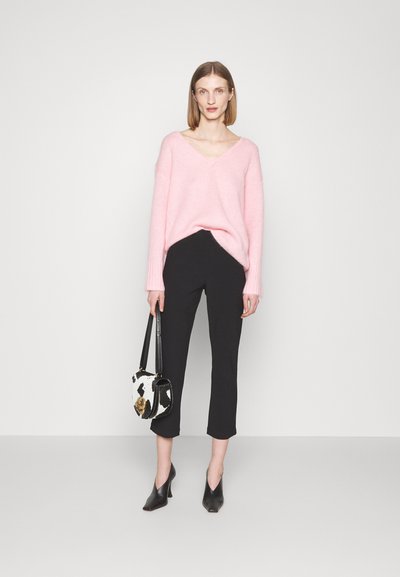 Light pink v-neck sweater, black cropped pants, black heeled shoes, and a black-and-white patterned handbag with a gold accent.
