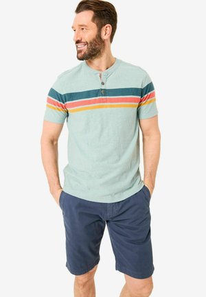 Light green short-sleeve shirt with multi-colored horizontal stripes, three-button placket, paired with navy blue shorts. Casual fit.